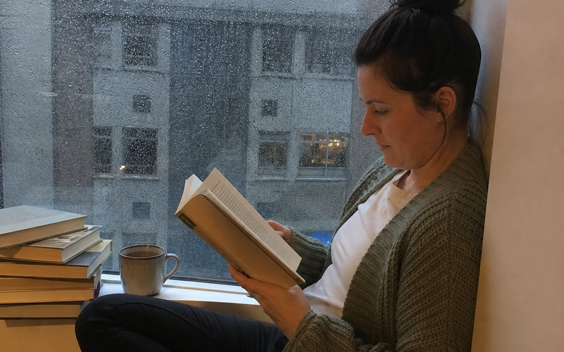 Frau liest an einem regnerischen Fenster – editoriale OBELLU Bildwelt