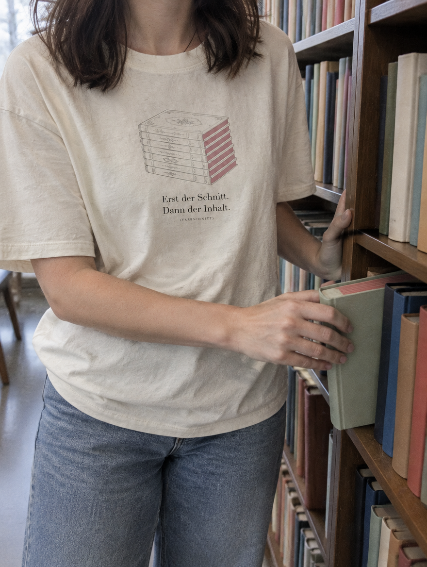 Nahaufnahme des Shirt-Drucks Erst der Schnitt. Dann der Inhalt. am Bücherregal