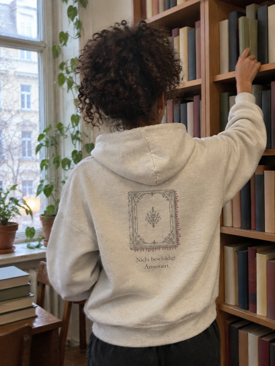Frau von hinten am Bücherregal, trägt einen Hoodie mit Rückendruck Nicht beschädigt. Annotiert.