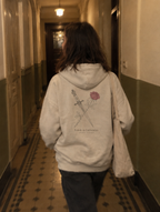 Frau von hinten im Altbauflur, trägt einen Hoodie mit Rückendruck Dolch und Rose, Feinde zu Liebenden