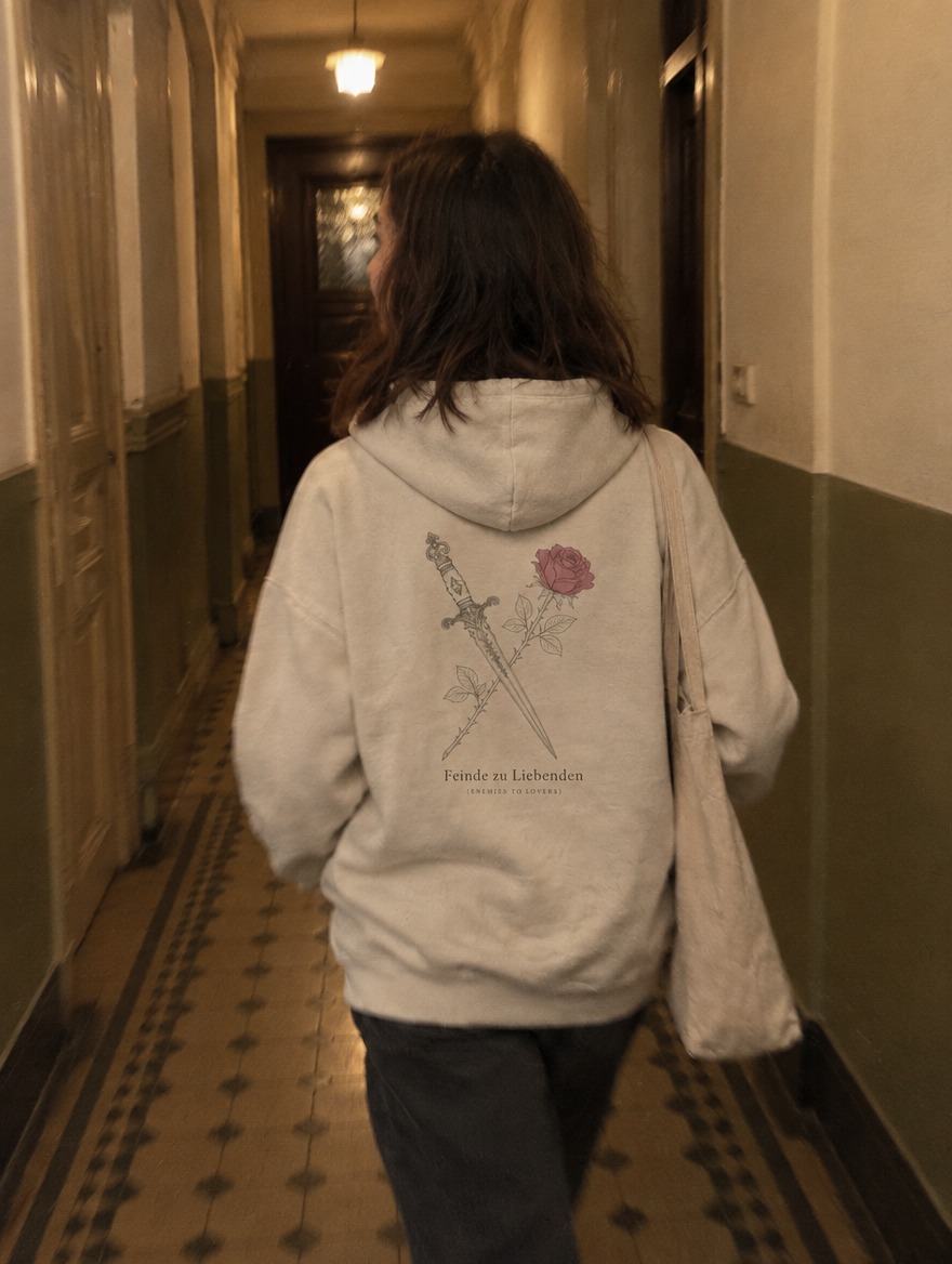 Frau von hinten im Altbauflur, trägt einen Hoodie mit Rückendruck Dolch und Rose, Feinde zu Liebenden